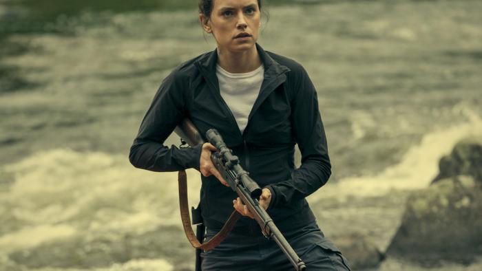 The Marsh King's Daughter Movie: Daisy Ridley holds a rifle at the ready while standing next to a canoe in the nature