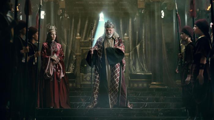 Mary: Anthony Hopkins stands in front of a large gold throne, Stephanie Nur to his side, and attendants lined up in front of him
