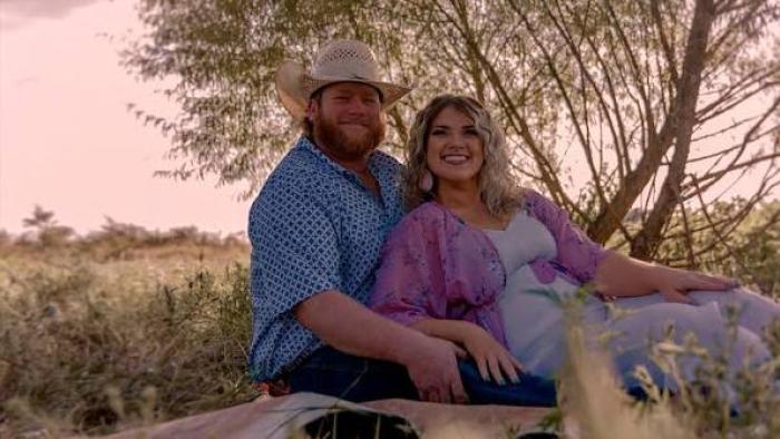Maternal Instinct movie: Couple sitting on a blanket in a field, smiling at sunset.