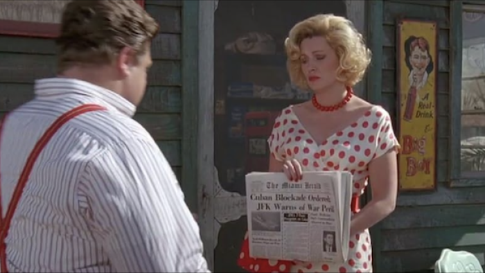 Matinee: Woman in polka dot dress holds a newspaper for a man to read