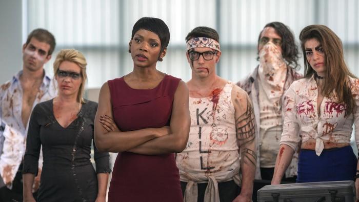 Mayhem: A woman stands in front of a band of bloodied and crazed-looking workers in an office building