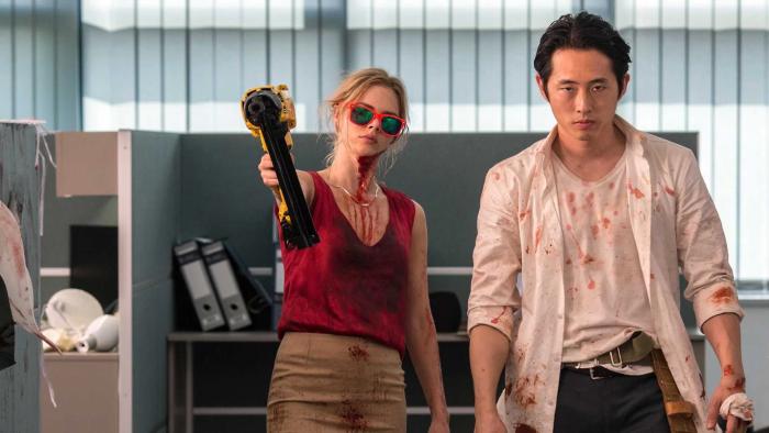 Mayhem: Woman in red holding a weapon, man beside her, both with blood stains in an office setting