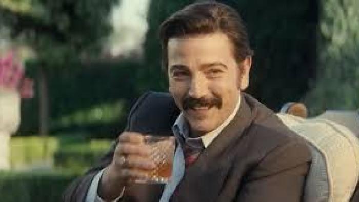 Mexico 86 Movie: Diego Luna smiling, holding a drink, sitting outdoors in a garden.