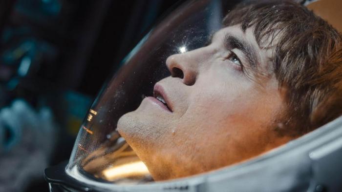 Mickey 17 Movie: Mickey (Robert Pattinson), in a spacesuit, looks upward at something bright, which shines on his face
