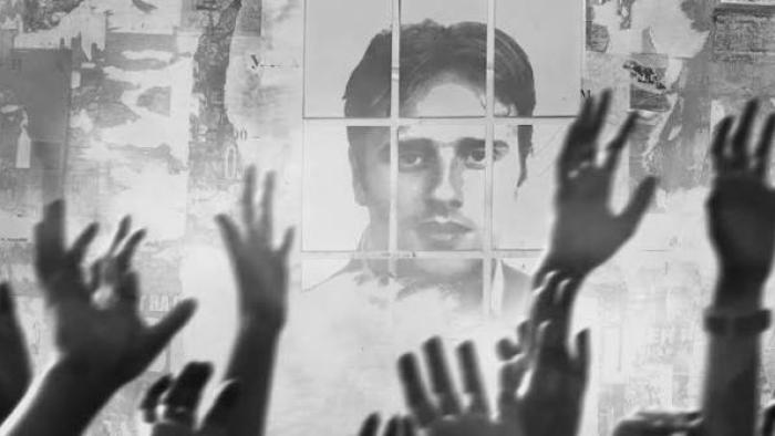 Miguel Ángel Blanco: The 48 Hours that Changed Spain Movie: Hands raised in front of a monochrome photo of a man's face on a wall.