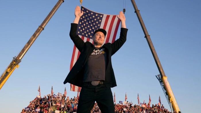 Musk movie: Elon musk stands in front of a crowd and the American flag