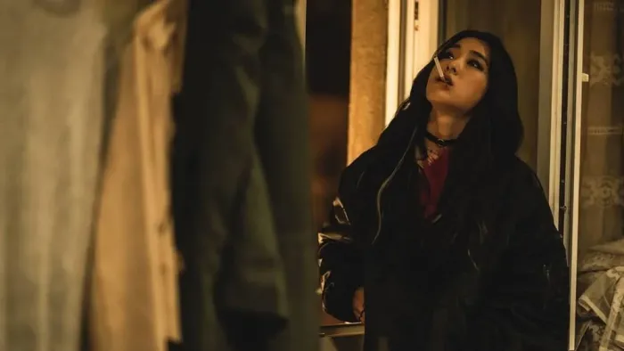 My Name is Loh Kiwan movie: Korean woman with long black hair in black jacket right looks upwards with cigarette in her mouth