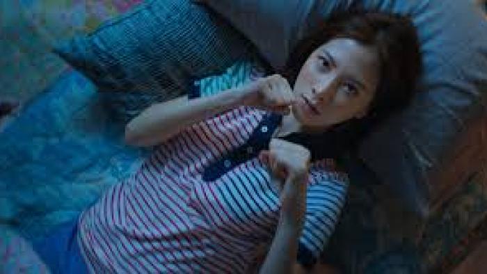 My Dearest Assassin: Woman lying on a bed, wearing a striped shirt, looking up thoughtfully.