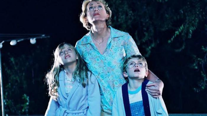 Mysterious Skin Movie: Woman and two children gazing at the night sky, wearing pajamas, with trees in the background.