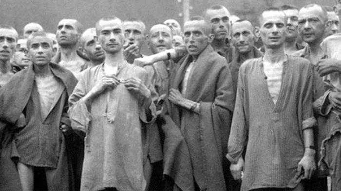 Night and Fog: A group of men stand huddled together, imprisoned in a concentration camp