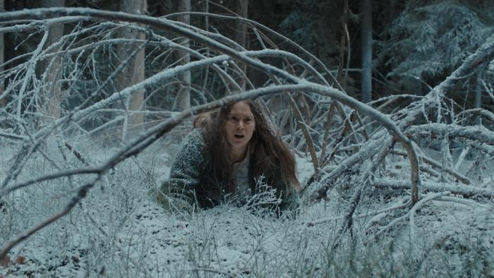 Nightborn: A young White woman crawling through snowy forest, branches overhead