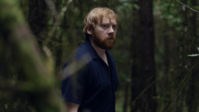 Nightborn: Red-haired man in a dark shirt stands in a dense, shadowy forest looking concerned
