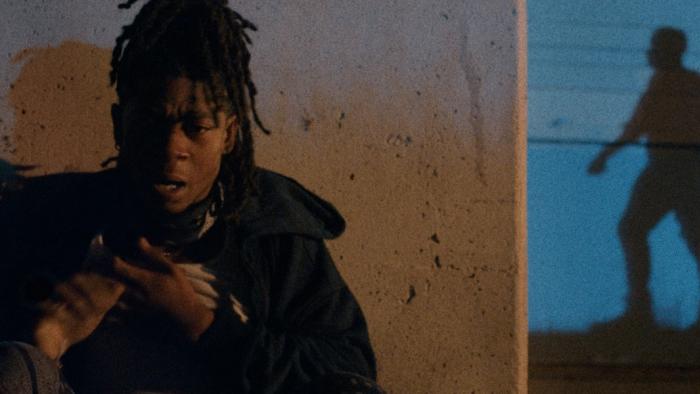 Night Patrol Movie: Wazi (RJ Cyler) hides up against a concrete wall while a sinister shadow appears to stalk him