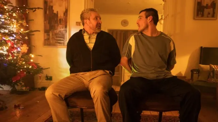 No Ordinary Heist: Two men sit tied to chairs in a warmly lit room near a Christmas tree