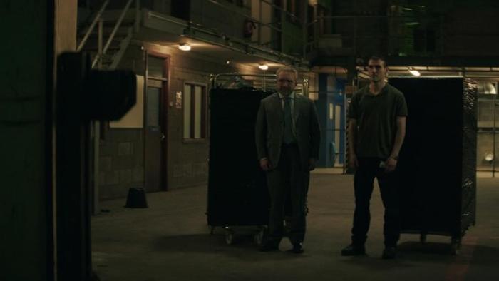 No Ordinary Heist: Dimly lit warehouse with two men standing between large carts