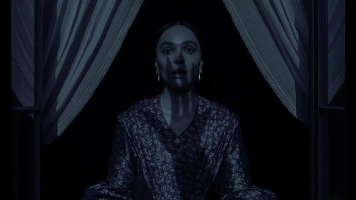 Nosferatu Movie: Ellen (Lily-Rose Depp) has a shocked expression as the shadow of a clawed hand crawls up her face