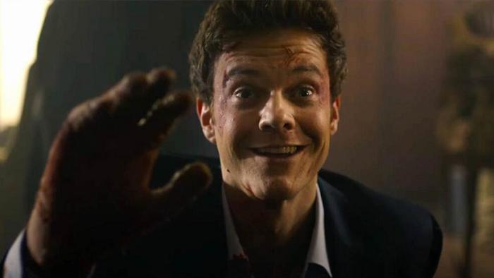 Novocaine Movie: Jack Quaid, some blood on his face, raises his hand and smiles in a way that looks desperate