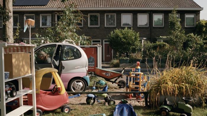 Occupied City Movie: A house with the view blocked by a yard filled with large children's toys and a tiny pink car