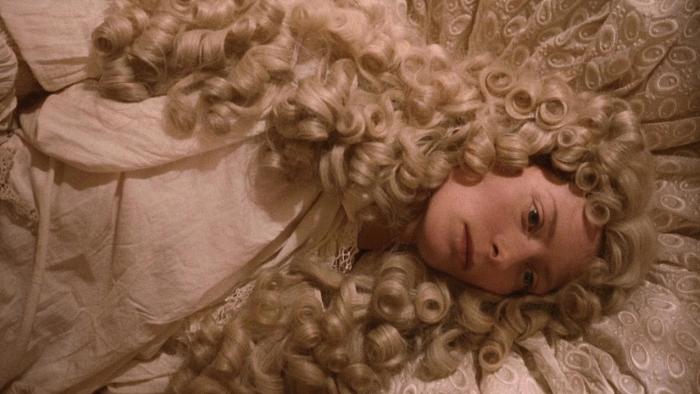 Orlando: Tilda Swinton lays down on a bed, her light blonde hair and white clothing blending into the lightly colored bedding