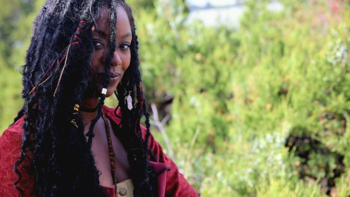 Outlaw Posse Movie: Singer and knife-slinger Queenie (Amber Reign Smith) smiles, wearing a red dress