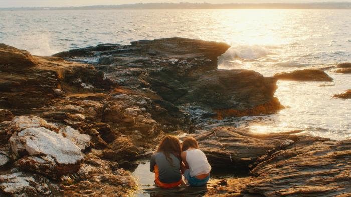 Over/Under: Two girls sitting on coastal rocks, watching the sunset over the ocean