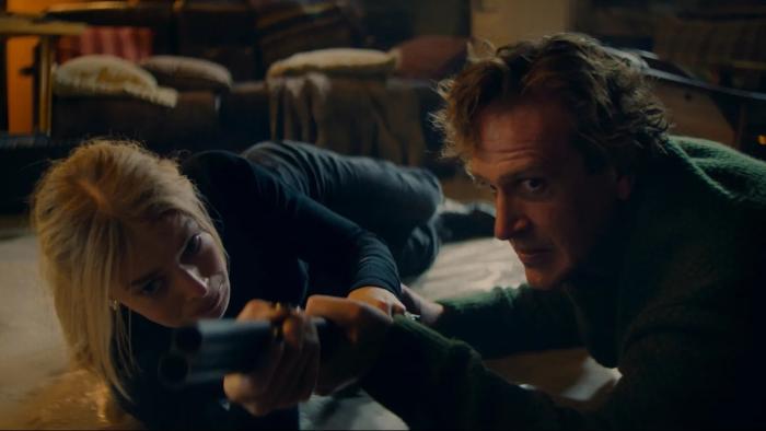 Over Your Dead Body movie: Samara Weaving and Jason Segel, lying on the floor, hold a shotgun and fight for control of it
