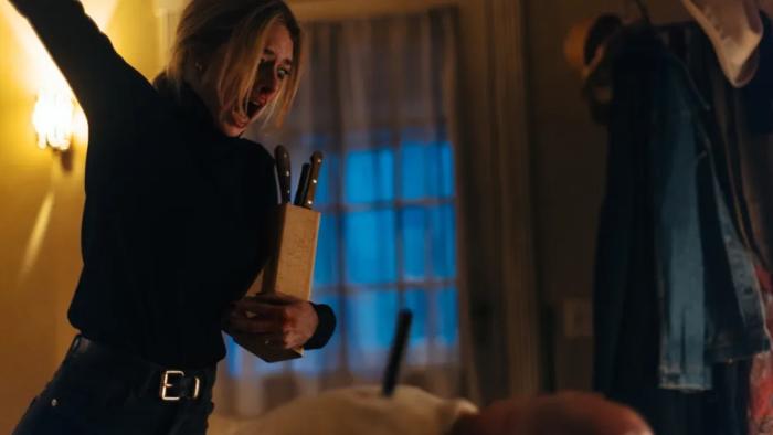 Over Your Dead Body movie: Samara Weaving holds knives in a dimly lit room, expressing anger