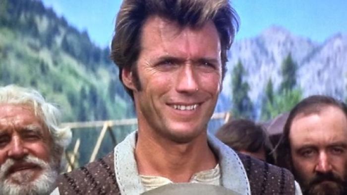 Paint Your Wagon: A White man with brown hair smiles, with two men behind him, one also smiling
