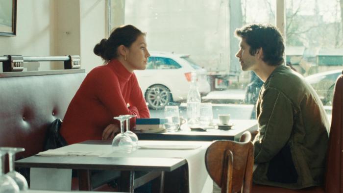 Passages: A young White woman sits opposite a White man at a cafe table by a window.