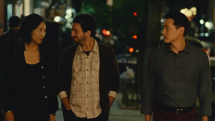 Past Lives: a Korean woman is walking with a White man close to her with an Asian man walking next to them both with a wistful look on his face