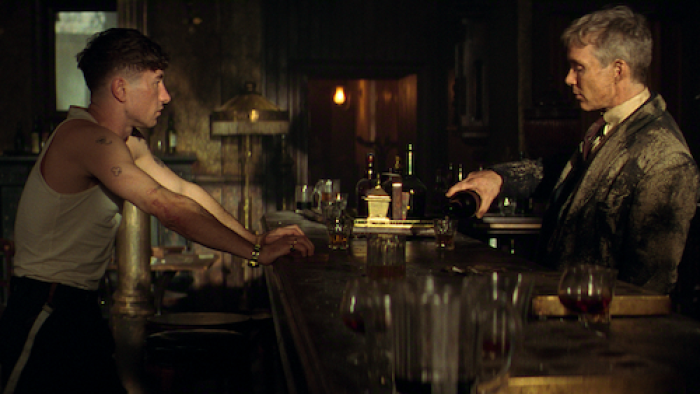 Barry Keoghan and Cillian Murphy face each other across a dimly lit bar in a tense scene from Peaky Blinders: The Immortal Man