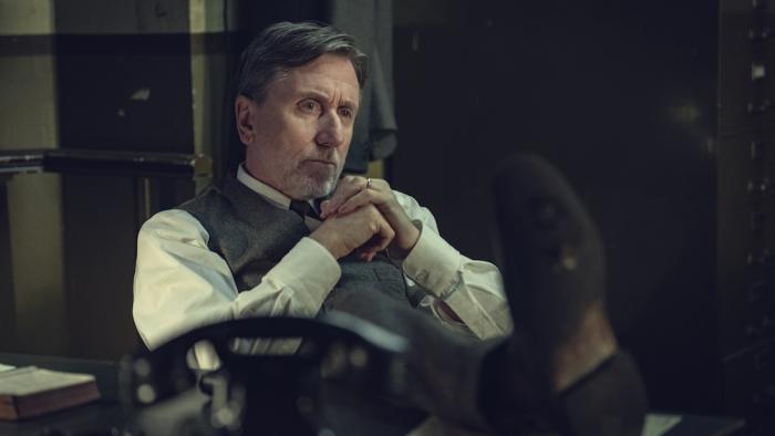 A man in a waistcoat and shirt sits pensively at a desk in a dimly-lit office in Peaky Blinders: The Immortal Man