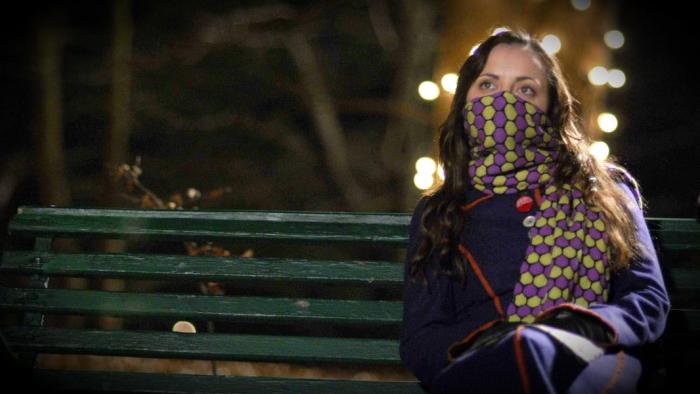 Christina Ricci wears a scarf over her face and sits on a green park bench.