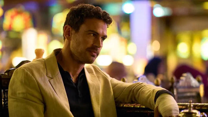 Fuze: A man in a cream blazer over a black shirt sits relaxed at what appears to be a bar or casino, with colorful bokeh lights in the background