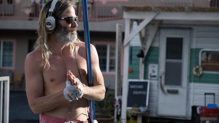 Poolman Movie: Shirtless Darren wears sunglasses and CD Walkman headphones while holding his pool-scooper