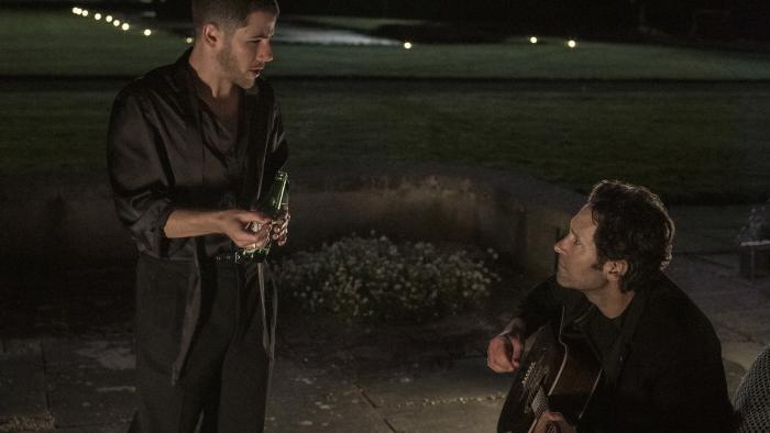Power Ballad movie: Outside at night, pop singer Danny (Nick Jonas) holds a beer and chats with Rick Power (Paul Rudd), who sits playing the guitar