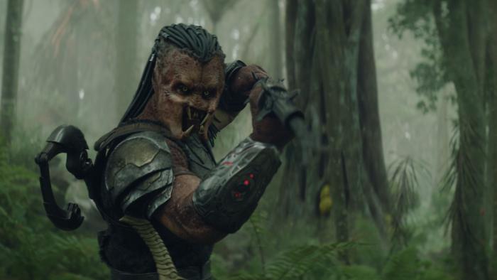 Predator: Badlands Movie: On a misty green forest planet, Dek holds his weapon at the ready