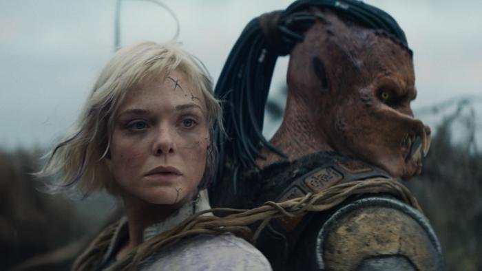 Predator: Badlands Movie: Strapped to Dek's back, Thia (Elle Fanning) looks over at something with concern