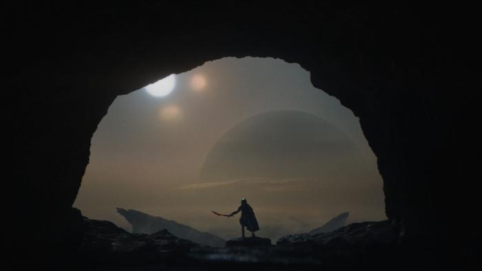 Predator: Badlands Movie: Dek, framed by darkness, holds his sword at the ready as he enters the mouth of a cave