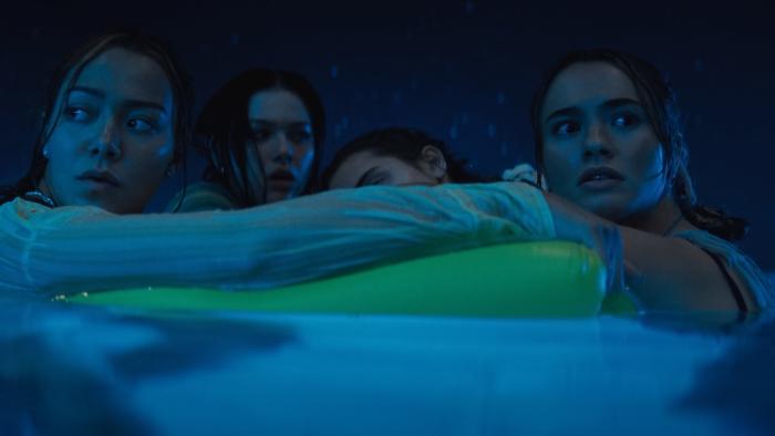 Primate Movie: Four women clutch a yellow float in a swimming pool, looking around leerily