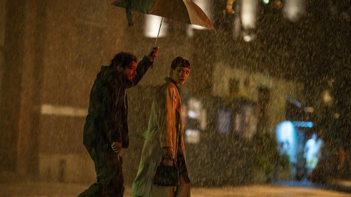 John Magaro holds an umbrella over the head of Britt Lower as they walk through the pouring rain