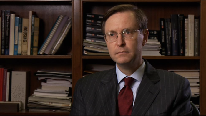 Inside Job: A White man sits in front of a bookshelf as he's interviewed