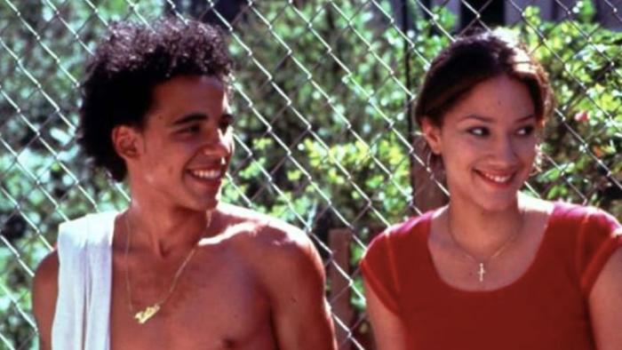 Raising Victor Vargas movie: Two young people smiling and laughing together outdoors by a chain-link fence.