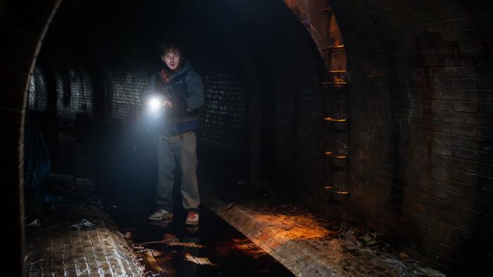 Resident Evil Movie: In a sewer with blood on the floor, Bryan holds a flashlight and reacts to something odd