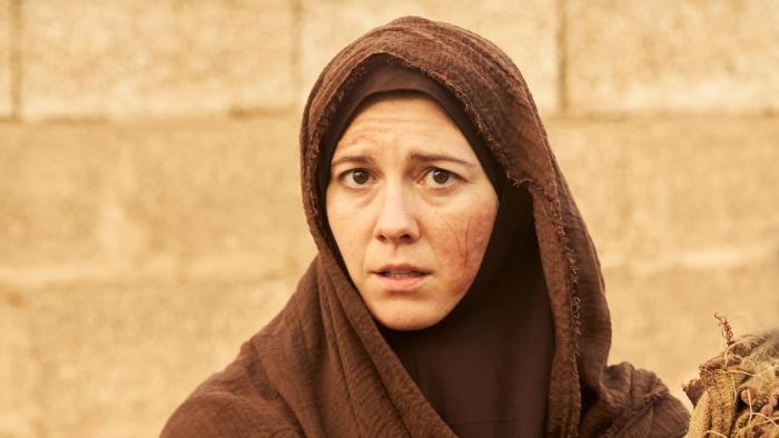 Rich Flu: Woman stands in front of a brick wall with a cut on her cheek, her head covered with an Islamic veil