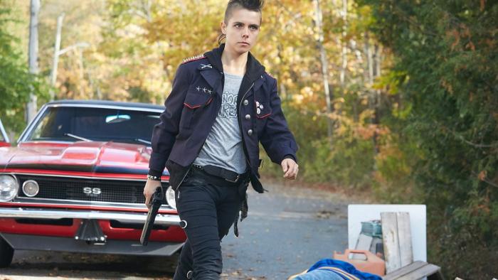 Riot Girls Movie: Scratch walks away from a red muscle car with a handgun