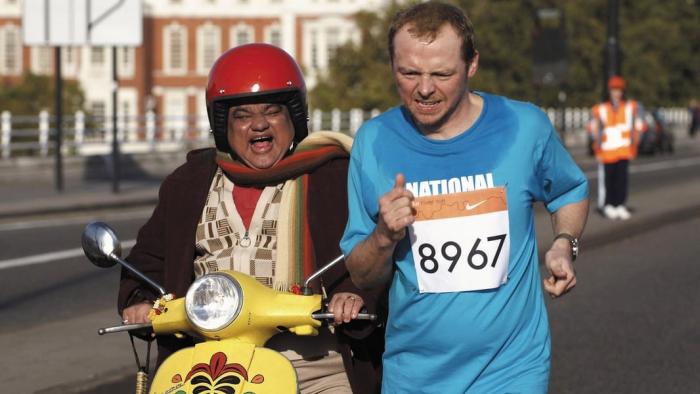 Harish Patel rides yellow moped while Simon Pegg runs alongside him, a marathon number stuck to his blue shirt.