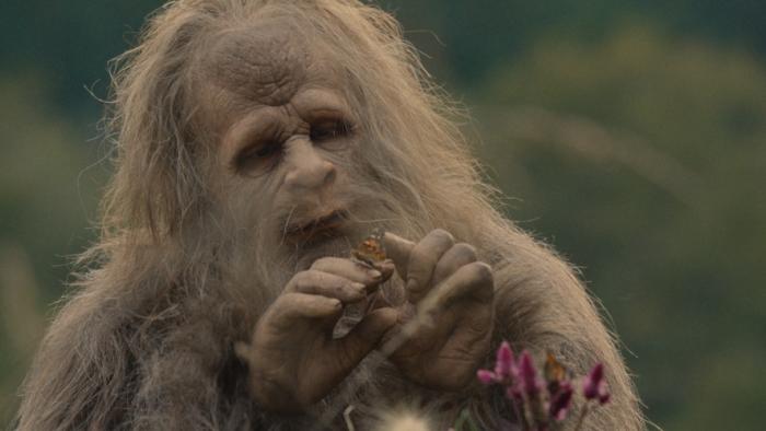 Sasquatch Sunset Movie: A Sasquatch (Jesse Eisenberg) contemplates a butterfly that sits on his finger
