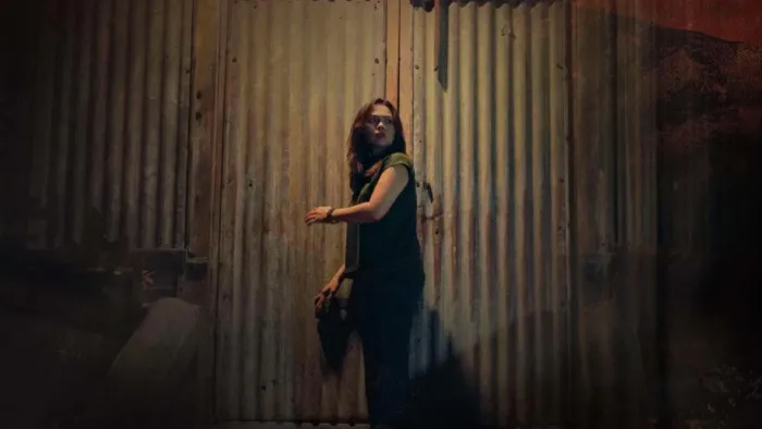 Scarecrow movie: Filipino woman with long black hair in sleeveless green shirt, center, looks behind her before going into a large farm shed