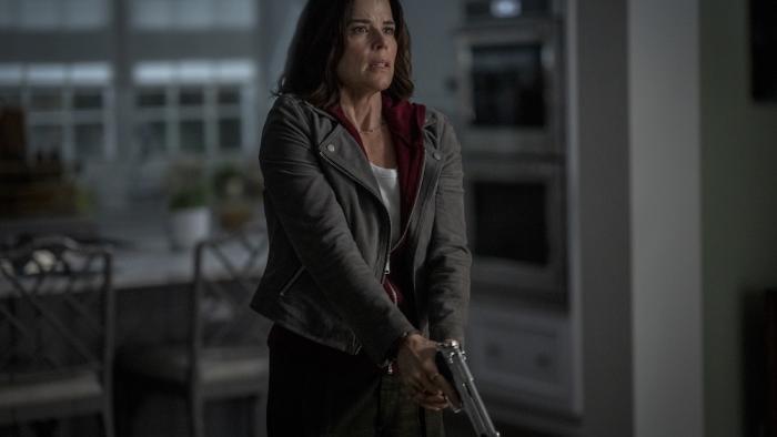 Scream 7 Movie: Looking shocked and tense, Sidney (Neve Campbell) clutches a gun with both hands, ready for anything